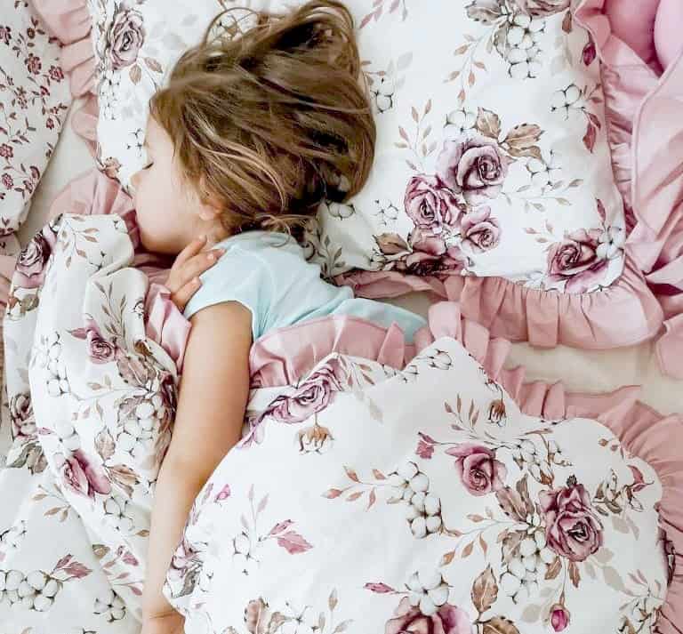 Niña durmiendo en cama con estampado de rosas